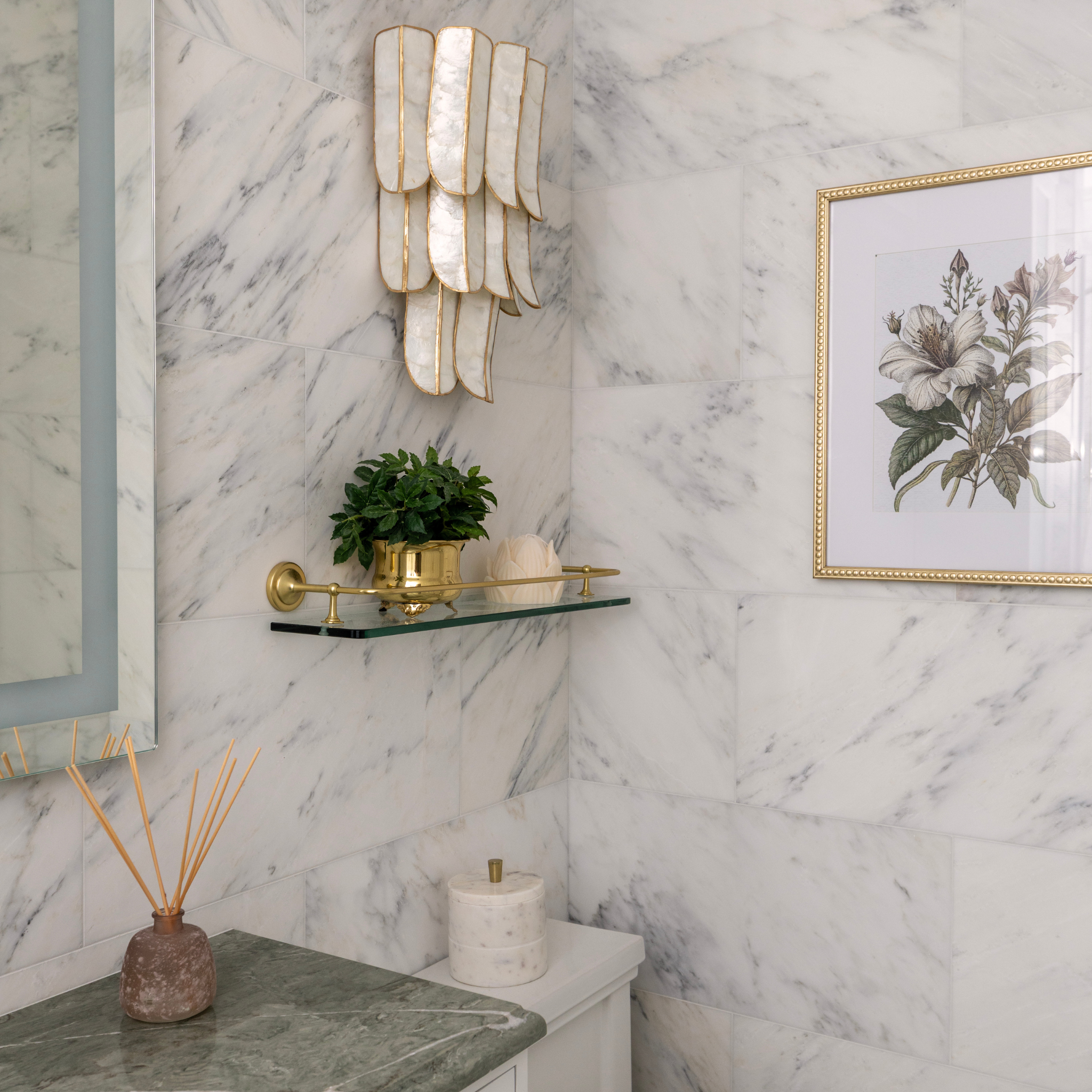 Bathroom interior with marble walls, decorative light fixture, plant, and artwork.
