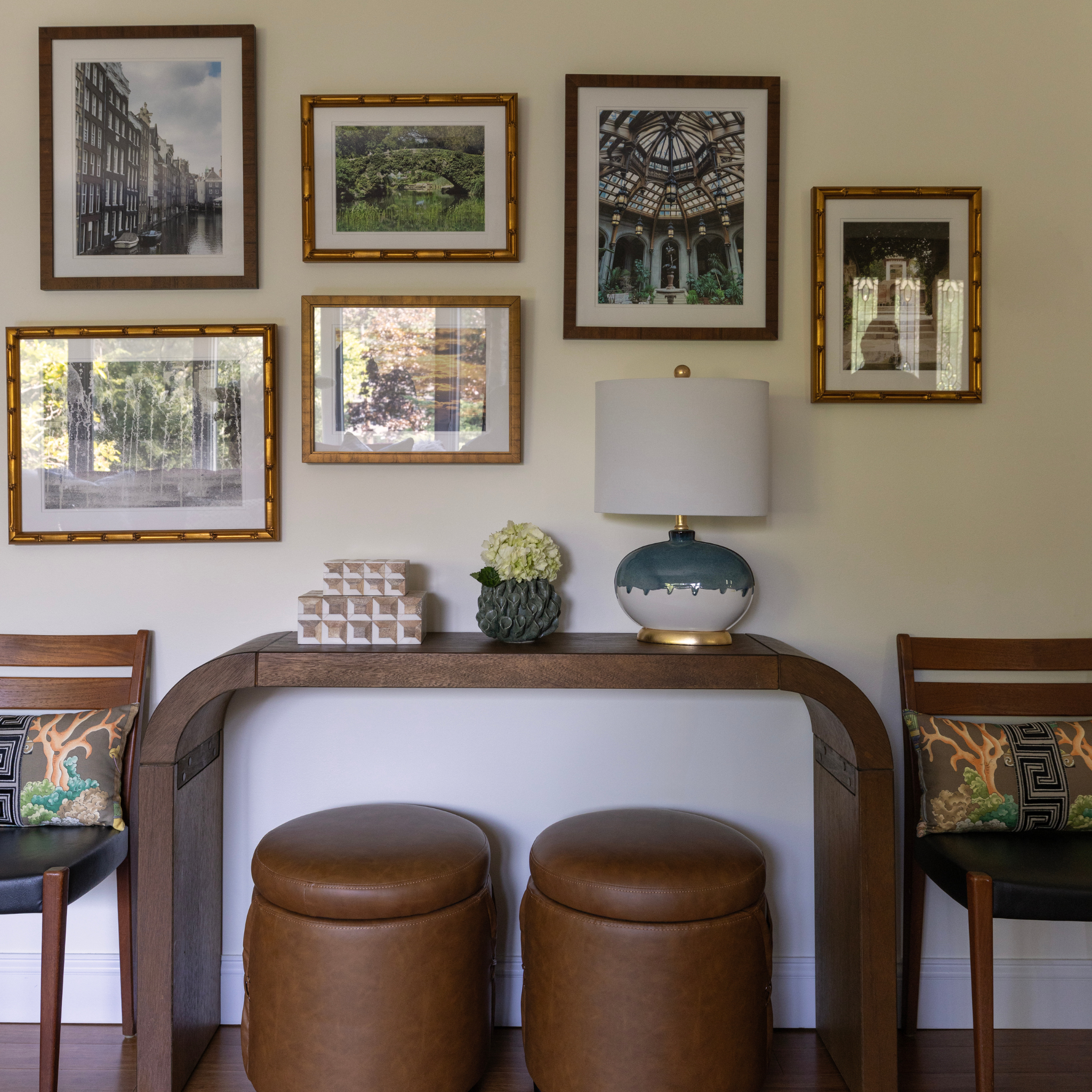 Dining area with framed pictures on the wall, a table with a lamp and decor items, and chairs with patterned cushions.