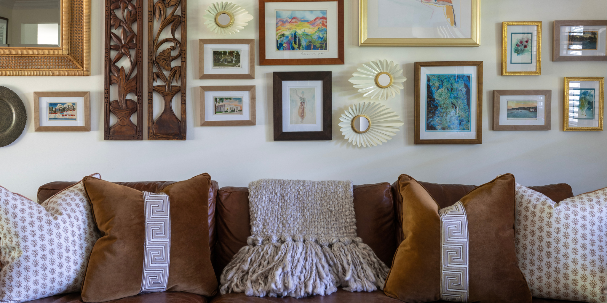 Wall with decorative items including framed pictures and a sunburst mirror, with a couch featuring patterned cushions.