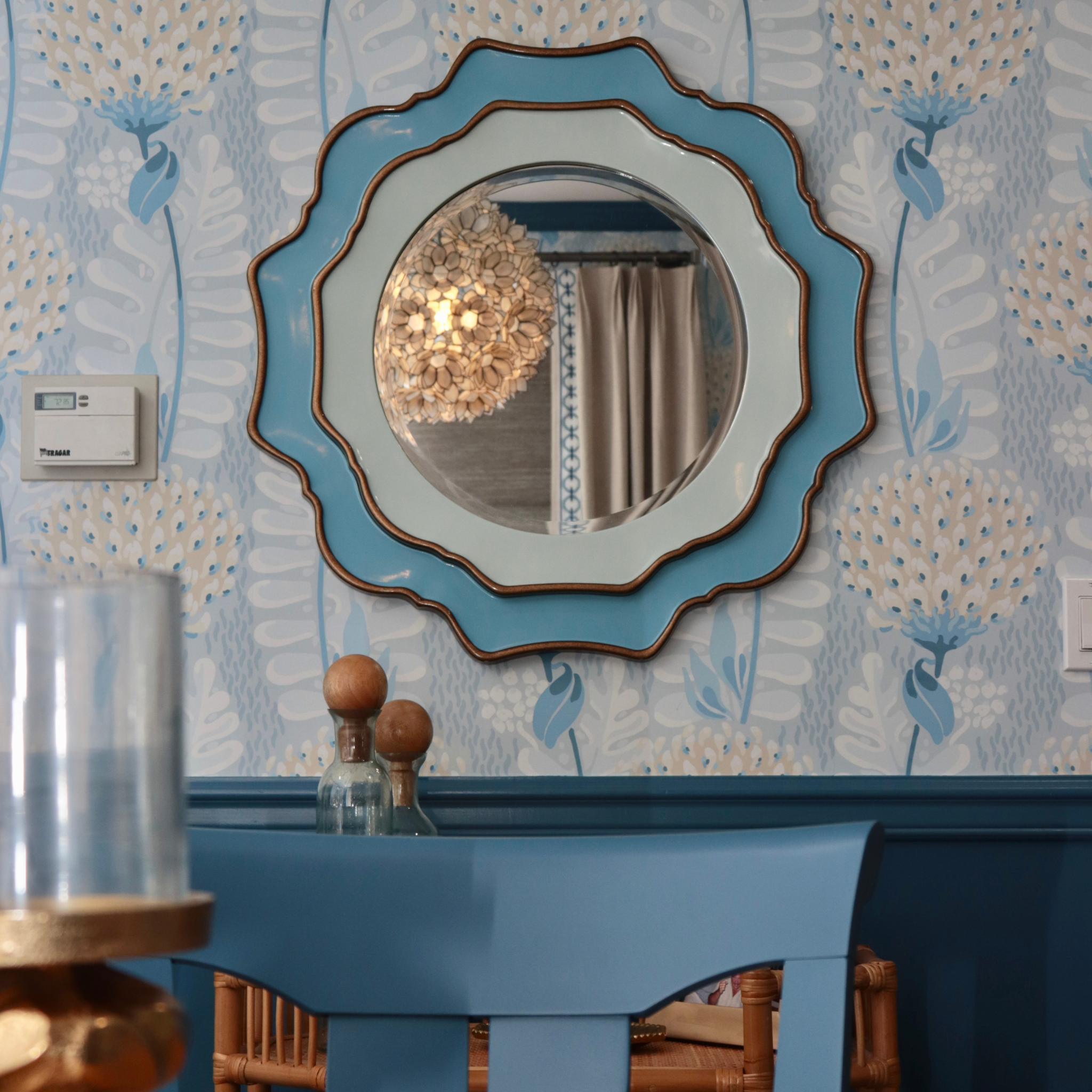 Decorative mirror with a blue floral-patterned wall in the background